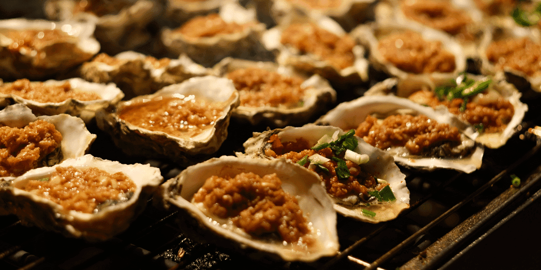 Grilled oysters topped with seasoned rice on a barbecue grill.