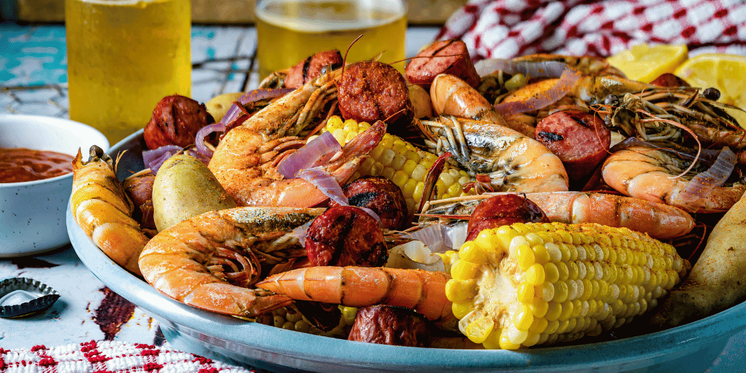 Bowl of shrimp, sausage, corn, and potatoes with drinks on a table.