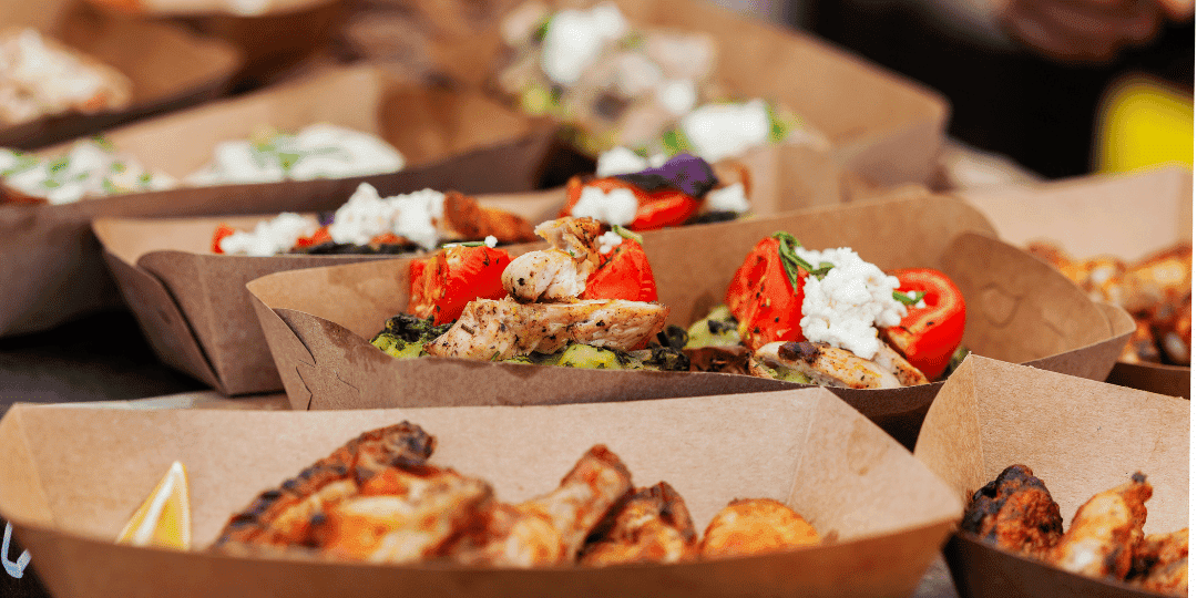 Street food market with trays of grilled meat, vegetables, and garnishes.